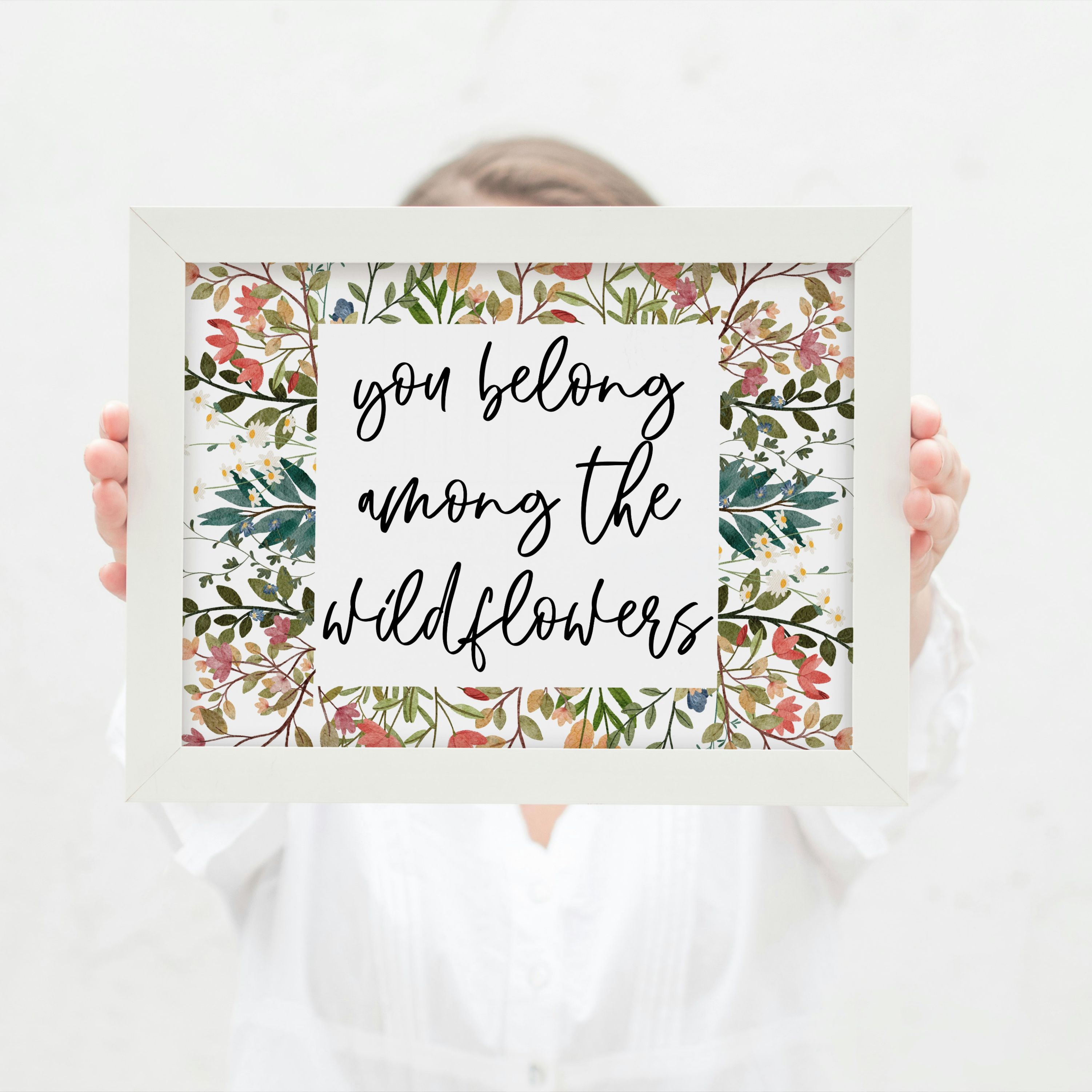 Person holding a framed print with 'you belong among the wildflowers' text and floral design.