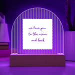 A wooden arch-shaped acrylic plaque with green and white vertical stripes and a white sign reading 'we love you to the moon and back' lit with purple LED backlight