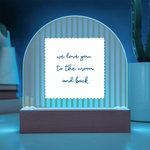 A wooden arch-shaped acrylic plaque with green and white vertical stripes and a white sign reading 'we love you to the moon and back' lit with a light blue LED backlight