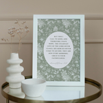 Decorative print with floral pattern and text on a table with a vase and bowl.