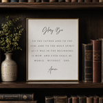 A framed typographic wall art print featuring the  Glory Be quote, displayed on a dark wooden bookshelf next to a vase with greenery and antique books.