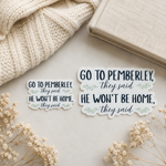 Two matching die-cut stickers with the text 'GO TO PEMBERLEY, they said HE WON'T BE HOME, they said' in dark navy script and small pale green floral accents, displayed on a light surface with a knitted cream scarf, a book, and dried flowers.
