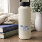 A cream-colored insulated water bottle with a black lid stands on a wooden table next to stacked books, with a knitted blanket and a potted plant in the background. The bottle features a printed quote in navy and gray text that reads, 'GO TO PEMBERLEY, they said, HE WON'T BE HOME, they said'.