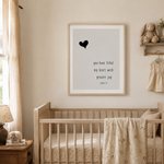 A framed nursery wall art print featuring a black heart and the quote 'you have filled my heart with greater joy psalm 1:7' in a light wood crib above, shown in a softly lit baby nursery with beige walls, curtains, and bedding.