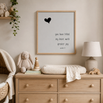 A framed nursery wall print with a black heart and the quote 'you have filled my heart with greater joy psalm 7:1' hangs above a light wood dresser in a styled nursery room with a bunny toy, lamp, and knit blanket.