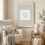 A framed art print with green and white vertical stripes and the text 'we love you to the moon and back' displayed on a beige wall in a styled nursery room setting.