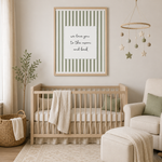 A framed nursery wall art print with sage green and white vertical stripes and the text 'we love you to the moon and back' hangs above a light wood crib in a softly styled nursery room.