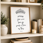A framed typographic art print with a crown illustration and the quote 'perhaps you were born for such a time as this.' displayed on a white shelf in a styled home setting with books, a candle, and plants.