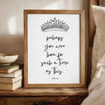 A framed typographic art print leaning on a wooden bedside table in a bedroom setting. The print features a black crown illustration and the quote 'perhaps you were born for such a time as this.