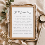 A framed print of The Ten Commandments styled in a flat lay with beige fabric, eucalyptus leaves, baby's breath, and a candle.
