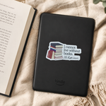 A black Kindle e-reader lying on a beige textured blanket next to an open book, with a sticker on the cover that reads 'I cannot live without books. My life starts with a book.